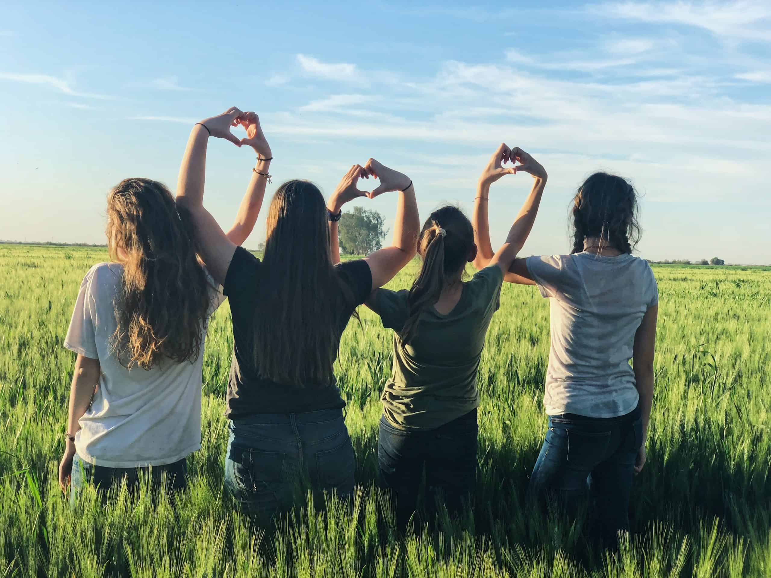 A group of women in a field forming heart shapes with their hands together