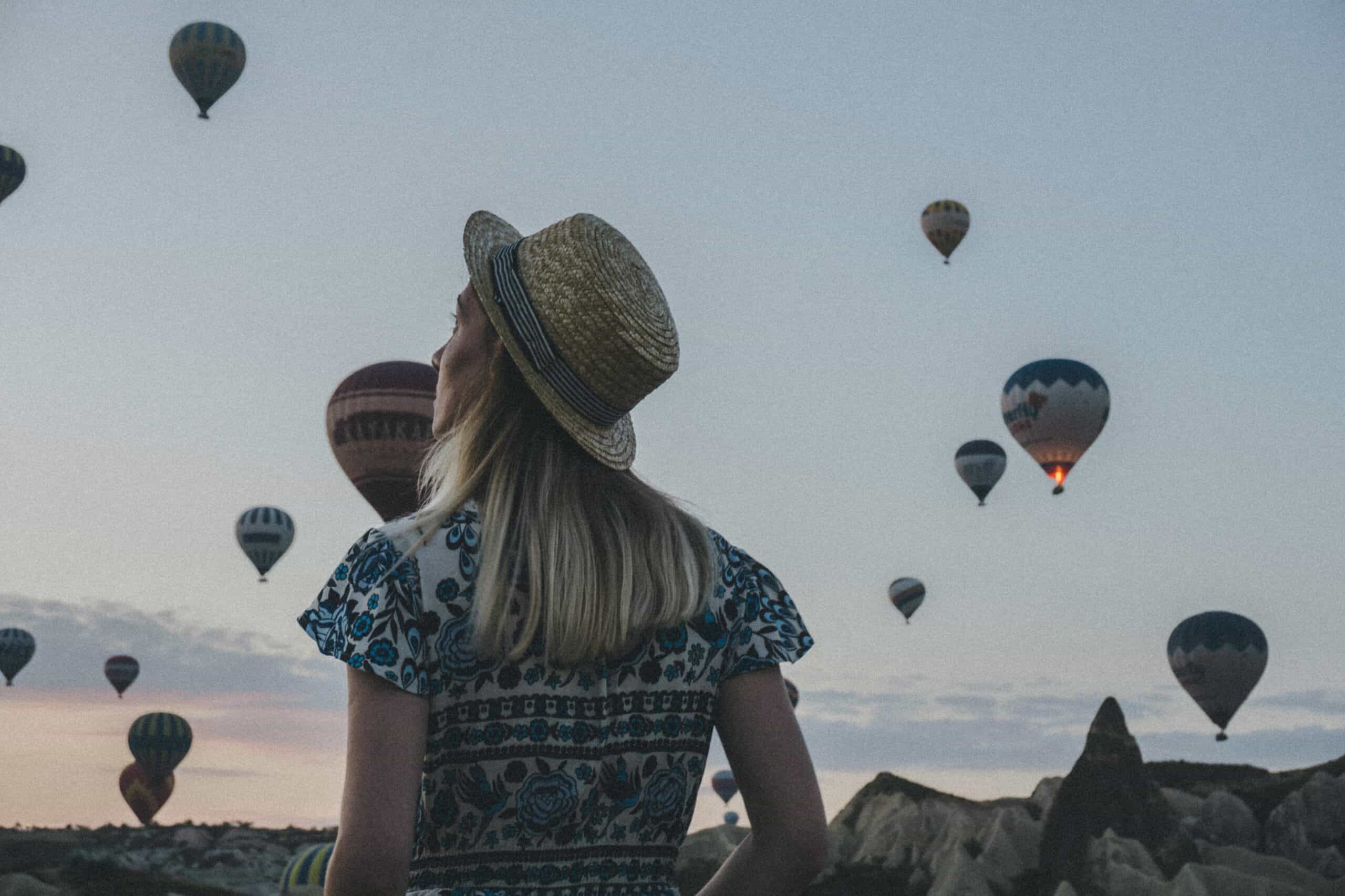 Woman wearing hat looking at hot air balloons taking off