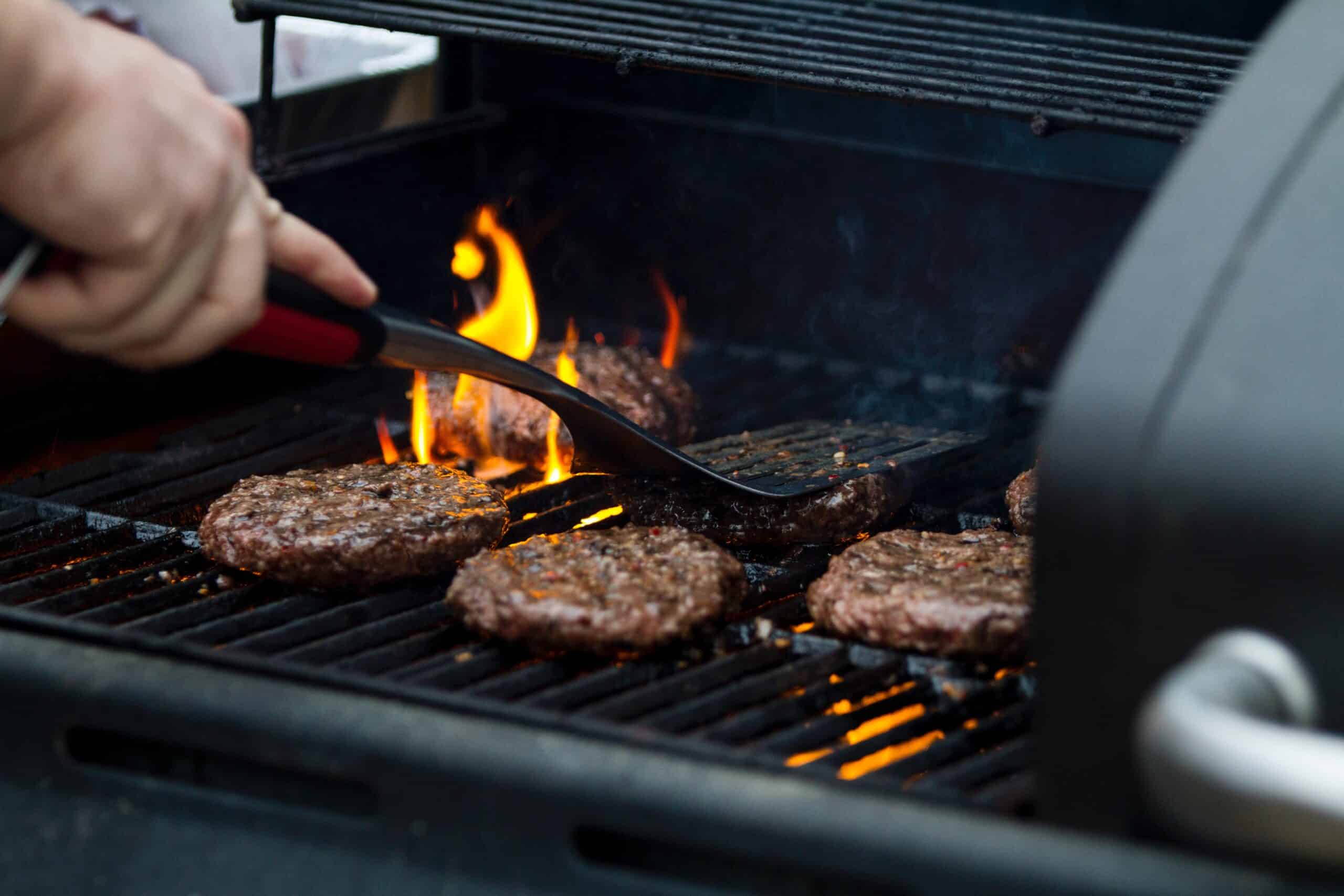 Person with spatula reaching toward burgers on a grill
