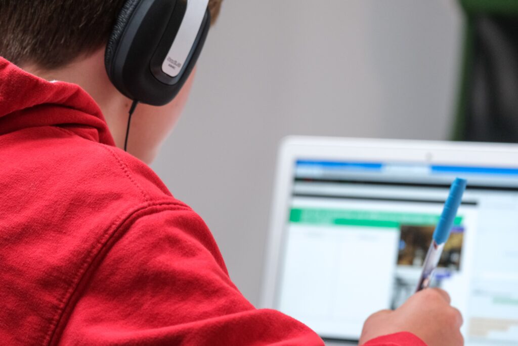 child wearing headphones holding pen looking at laptop screen