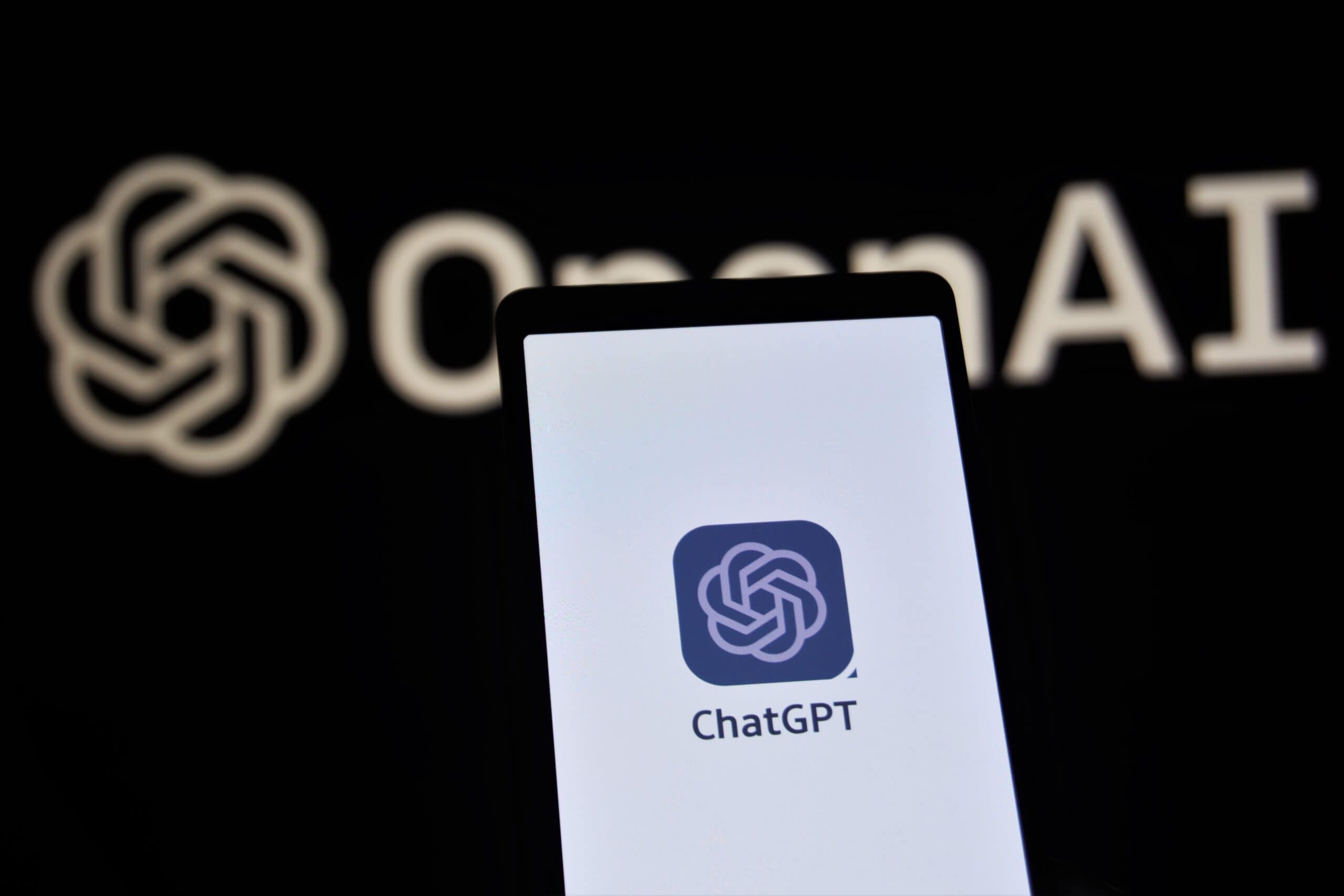 Phone with ChatGPT logo on screen in front of Open AI logo