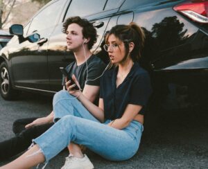 Man and woman leaning against a car wearing ear buds