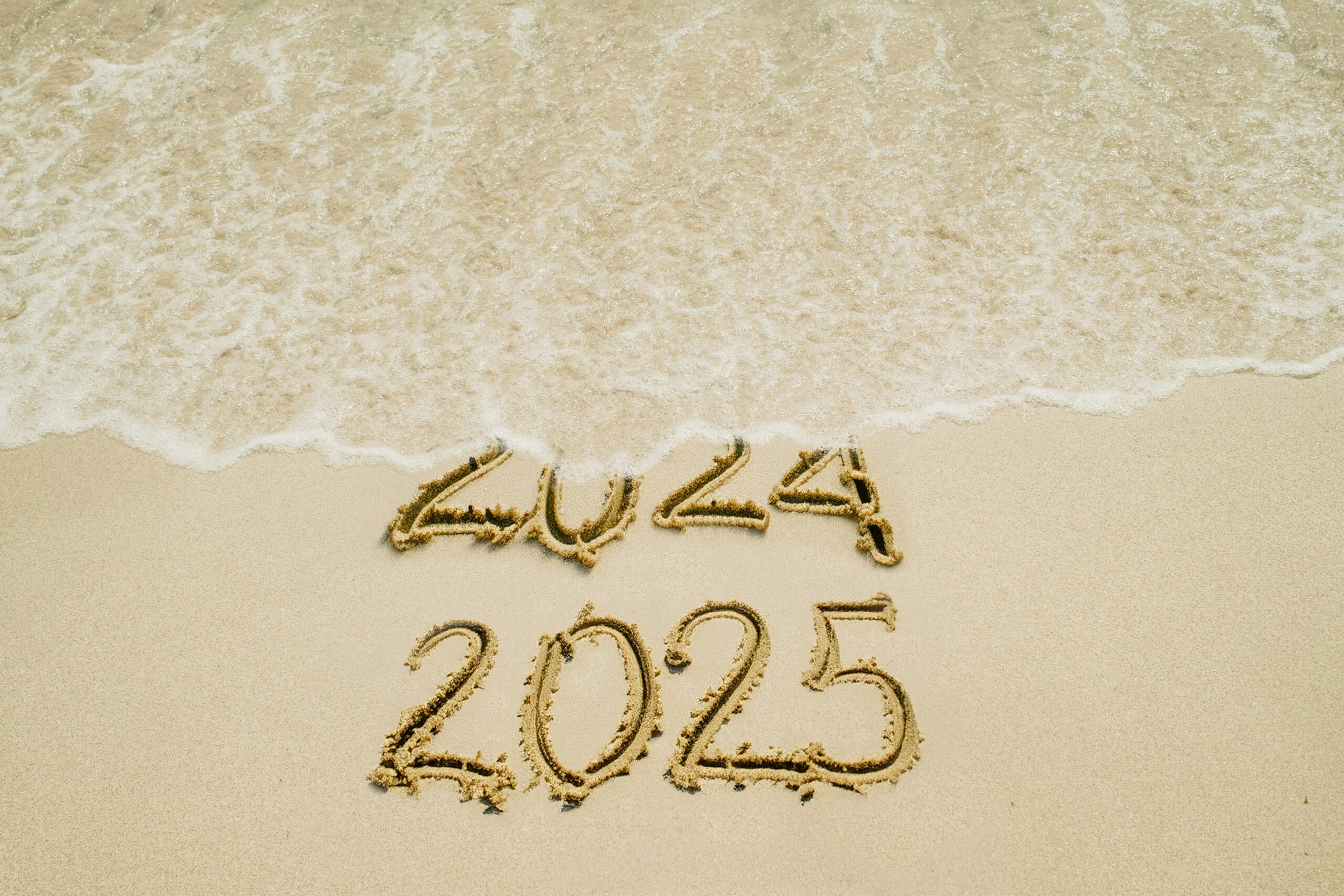 Image of 2024 ingrained in sand being covered by water in favor of 2025